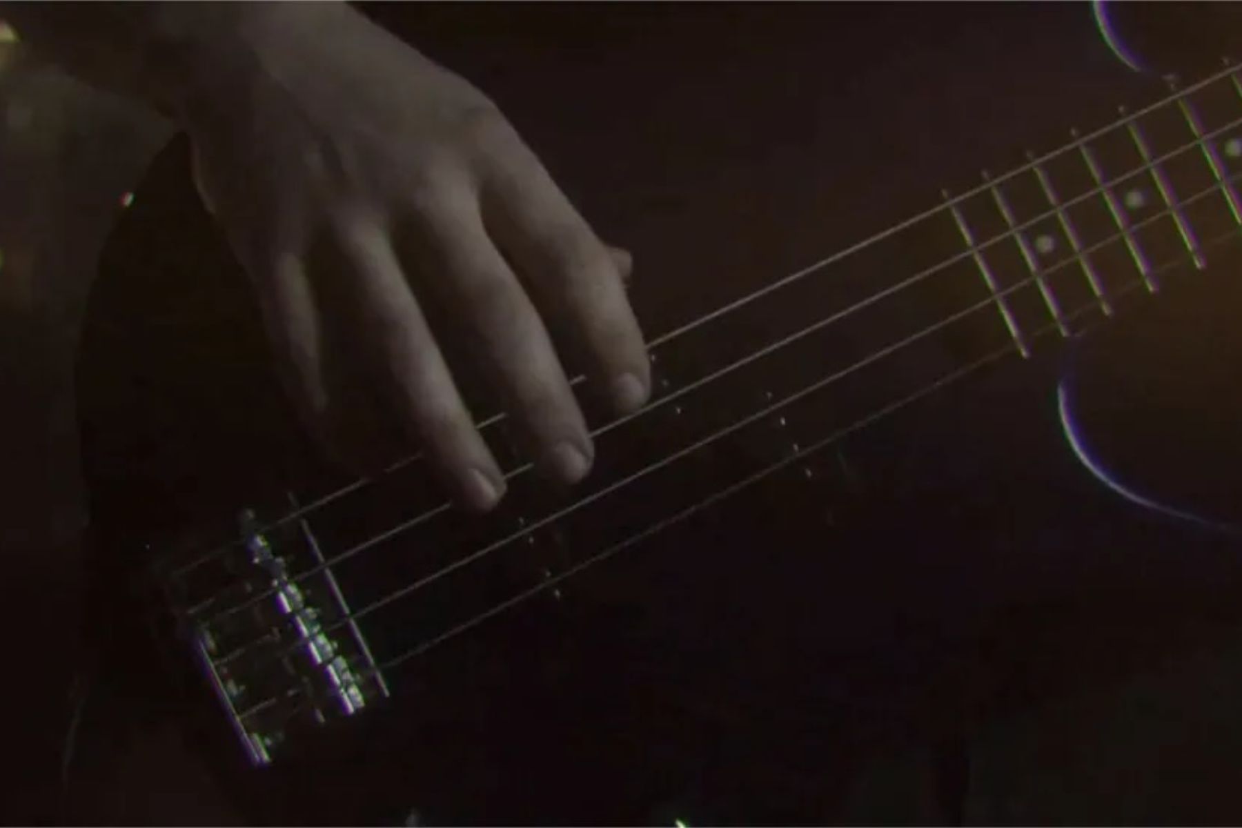 Close up on bass player's hand. Screenshot from the music video. Muted colors.