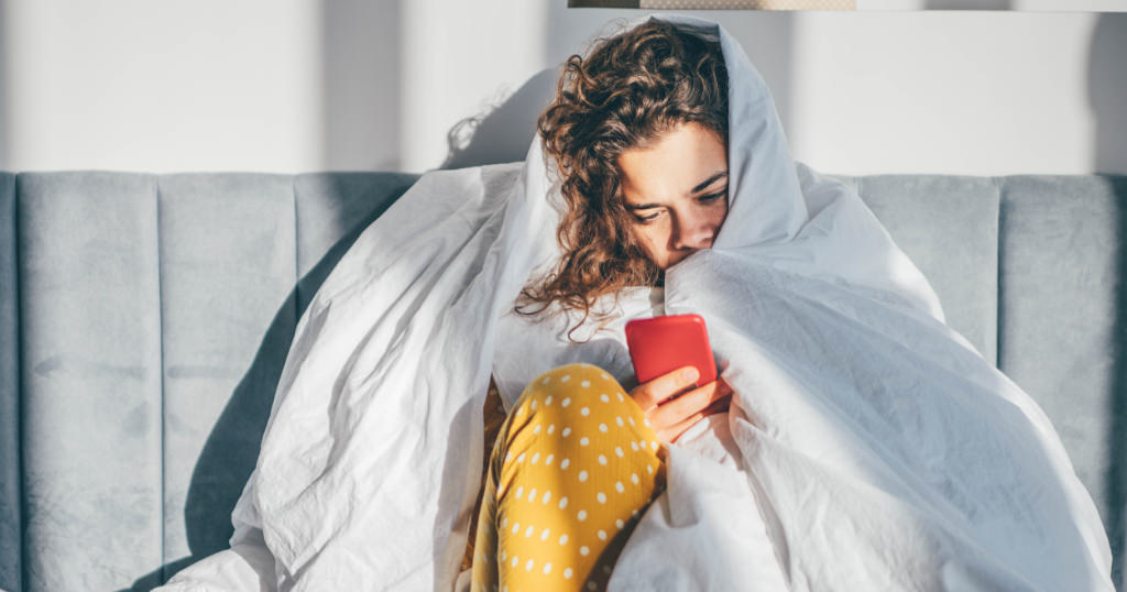 Woman looking at her phone covered in blankets